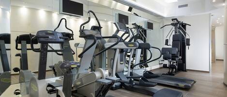 Un gimnasio moderno con diversas máquinas de cardio, un espejo grande y un televisor de pantalla plana.