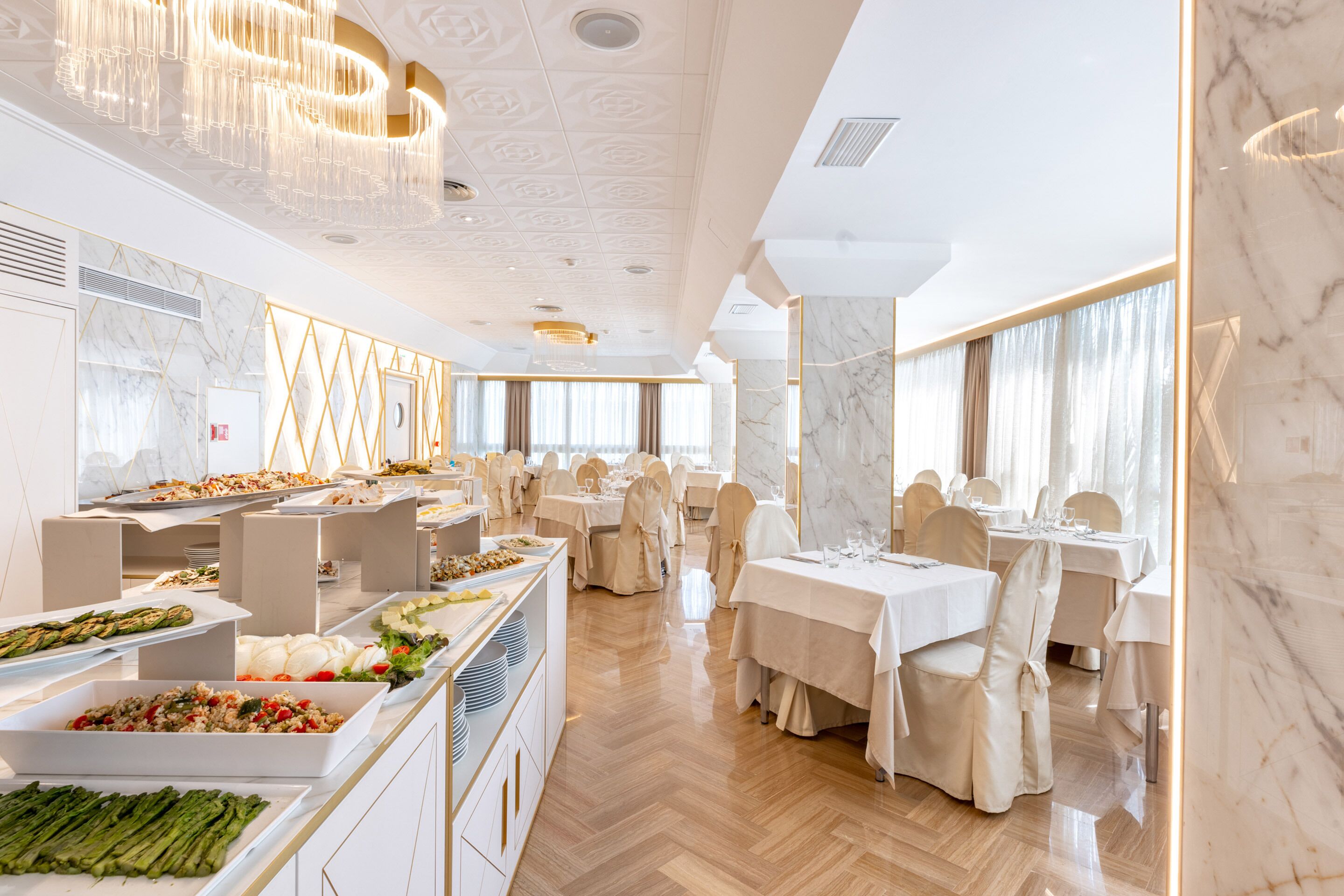 A spacious buffet area with multiple serving stations and tables set for dining, featuring marble walls and elegant lighting fixtures.