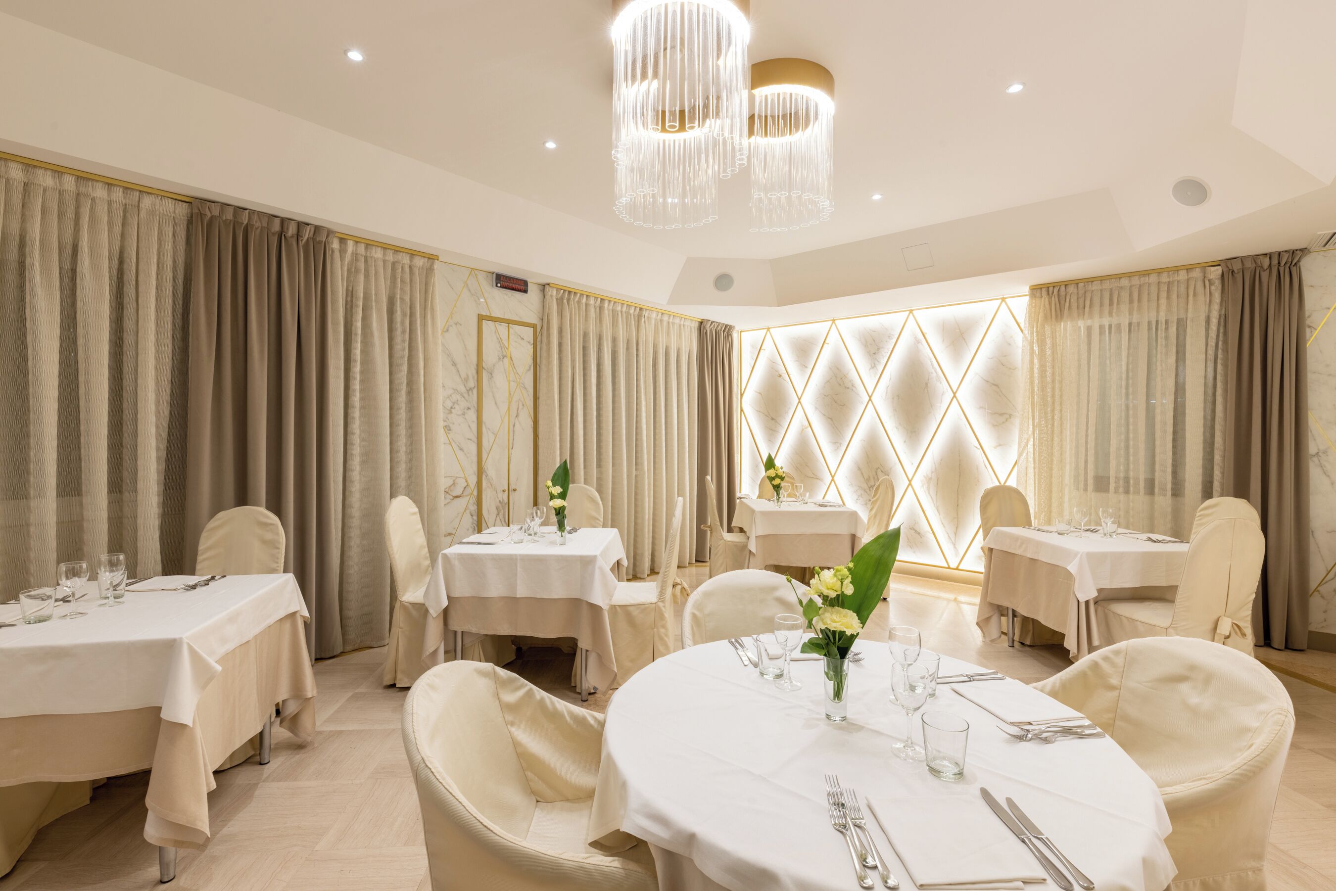 A dining area with round tables, white tablecloths, and beige chairs.