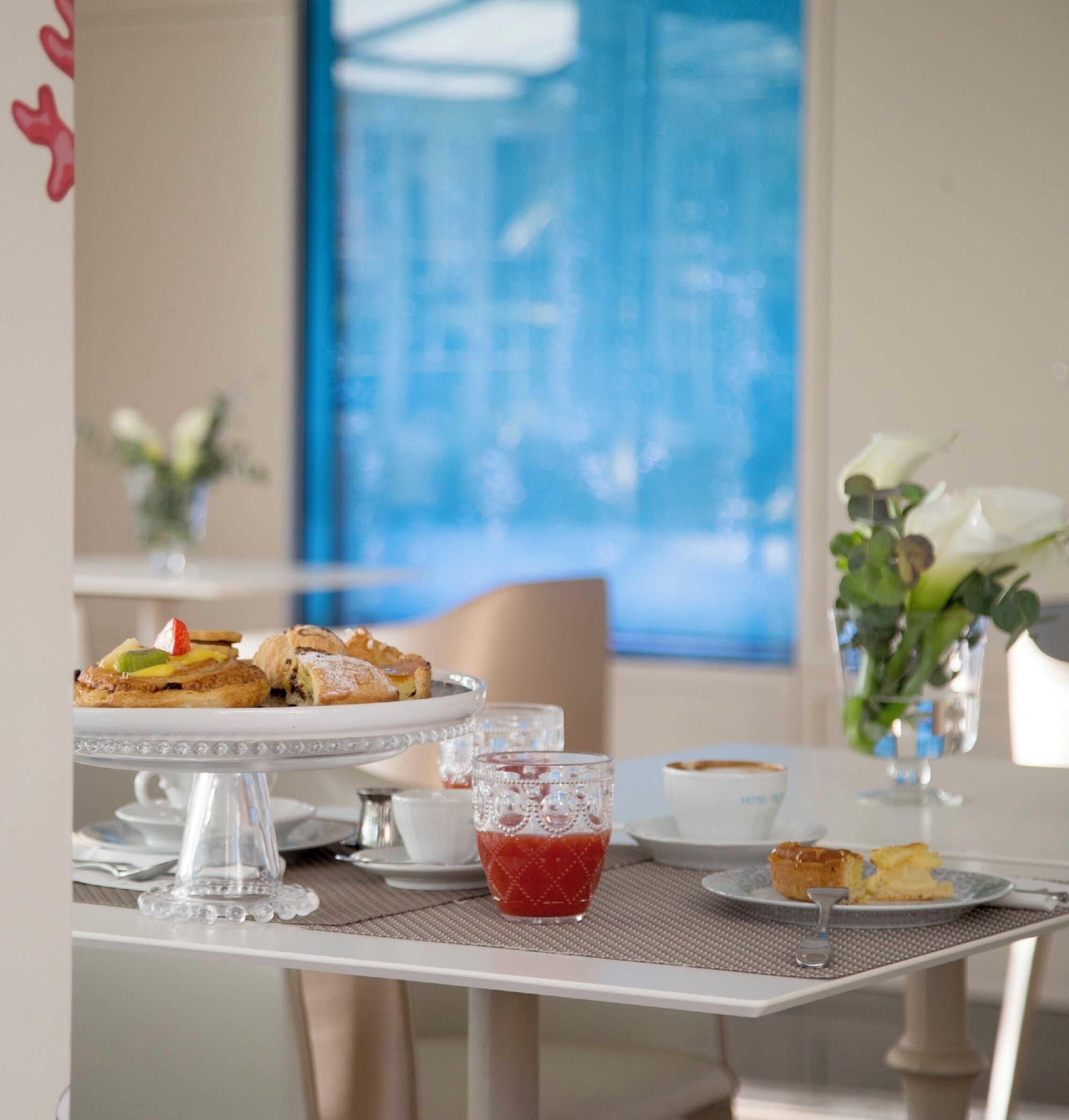 A dining table with a three-tiered dessert stand, a glass of red beverage, and a cup of coffee.