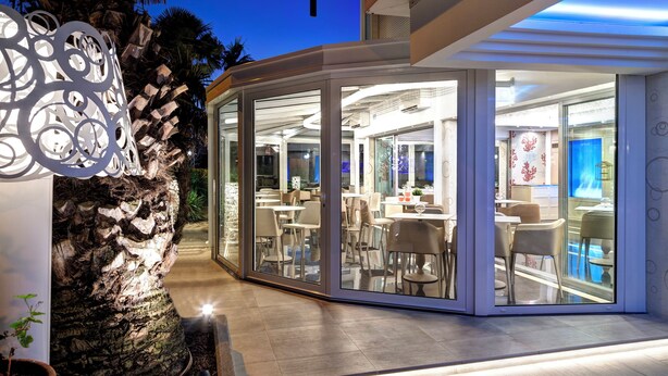 Un restaurante moderno con paredes de vidrio, una pared de piedra y un detalle decorativo de metal.