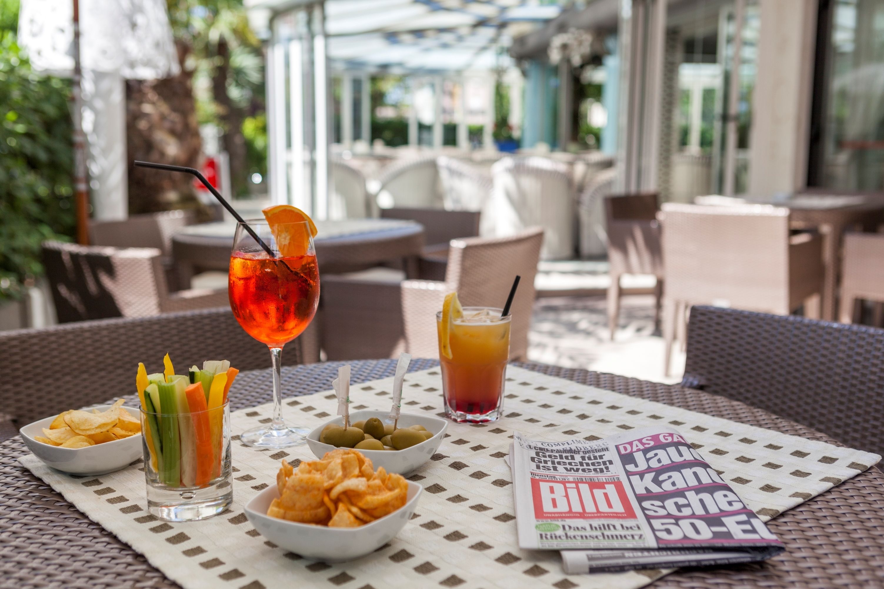 Area esterna con tavoli e sedie in vimini, un menu e un bicchiere di bevanda rossa guarnita con una fetta di limone.