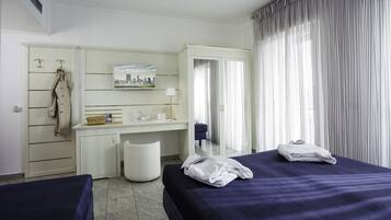 Habitación de hotel con dos camas, un escritorio, una silla, un armario y un ventanal con cortinas.