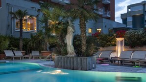 Una piscina con sillas de descanso y una estatua, rodeada de palmeras y plantas.