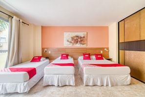 A hotel room with two single beds, each with a white mattress and red bedding, and a large window with beige curtains. - OYO Rio Colinas Hotel, Rio de Janeiro (Rio de Janeiro)