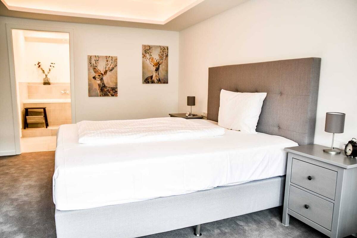Moderni hotellihuone, jossa on suuri sänky, yöpöytä lampun kanssa ja kaksi seinälle ripustettua peuran kuvaavaa taulua.
