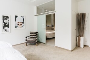 A bedroom with a bed, a patterned armchair, a mirror, and a bathroom visible through an open door. - Fritz am Brunnen (Schwelm)