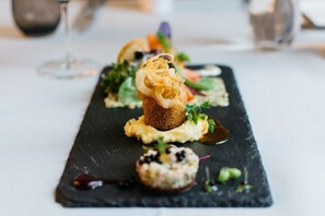 A black slate serving board with various appetizers, including a breaded item topped with onion rings, a small tart, and a dollop of cream with berries. - Fritz am Brunnen (Schwelm)