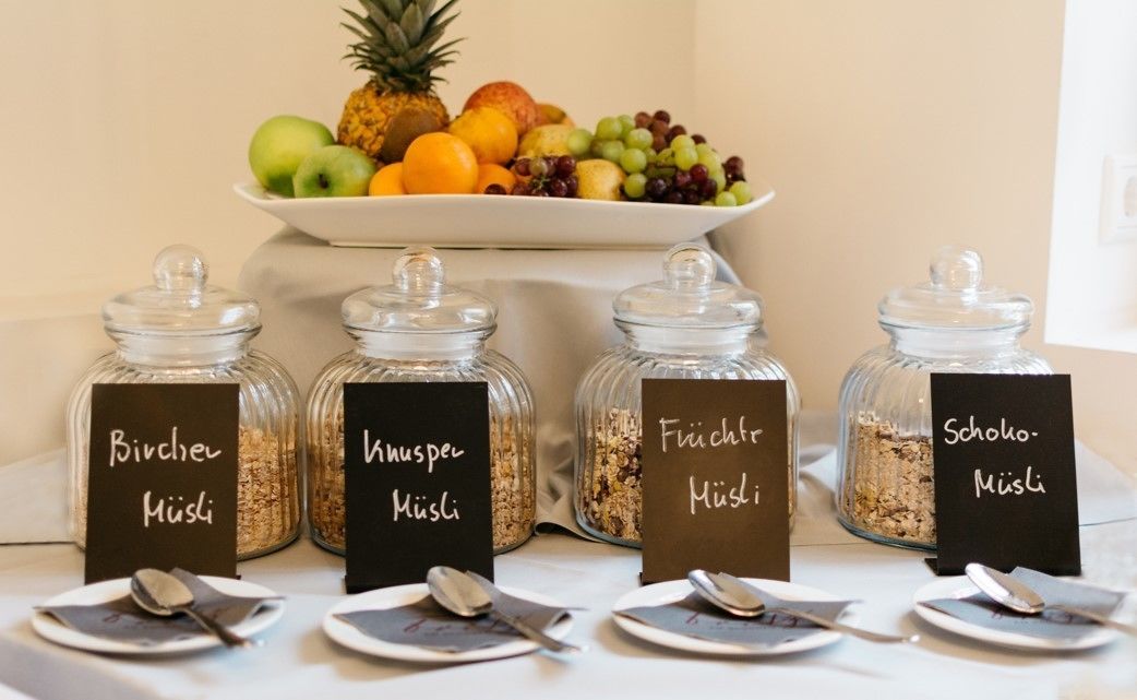 A buffet setup with labeled jars of Bircher Müsli, Wnuspener Müsli, Fruchtmüsli, and Schoko-Müsli.