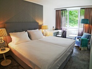 A hotel room with a large bed, a desk, a chair, and a view of greenery outside. - Fritz am Brunnen (Schwelm)