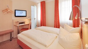 Habitació d'hotel amb un llit, una taula de treball amb una cadira, una televisió i una làmpada de taula.