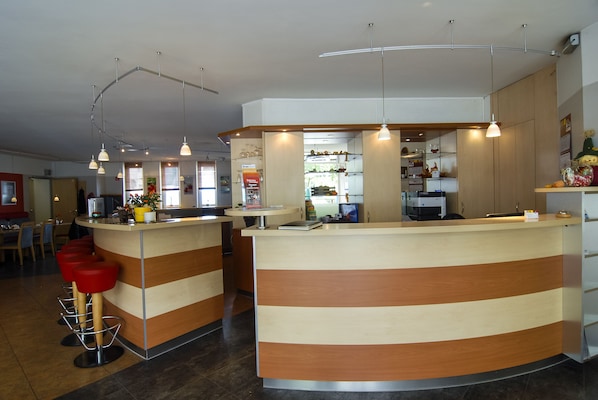 Un área de recepción moderna con mostrador curvo, taburetes rojos y una cocina a la vista al fondo.