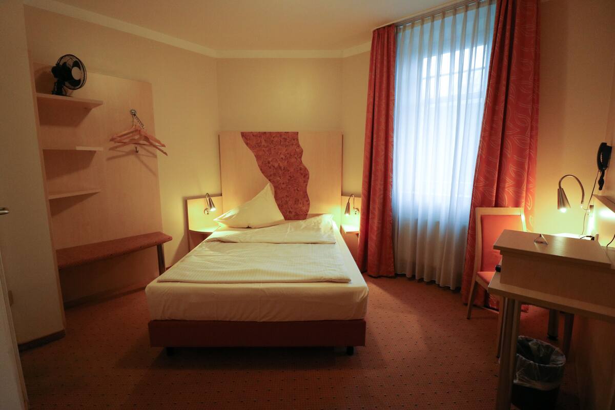 A hotel room with a bed, bedside tables, a desk, and a chair.