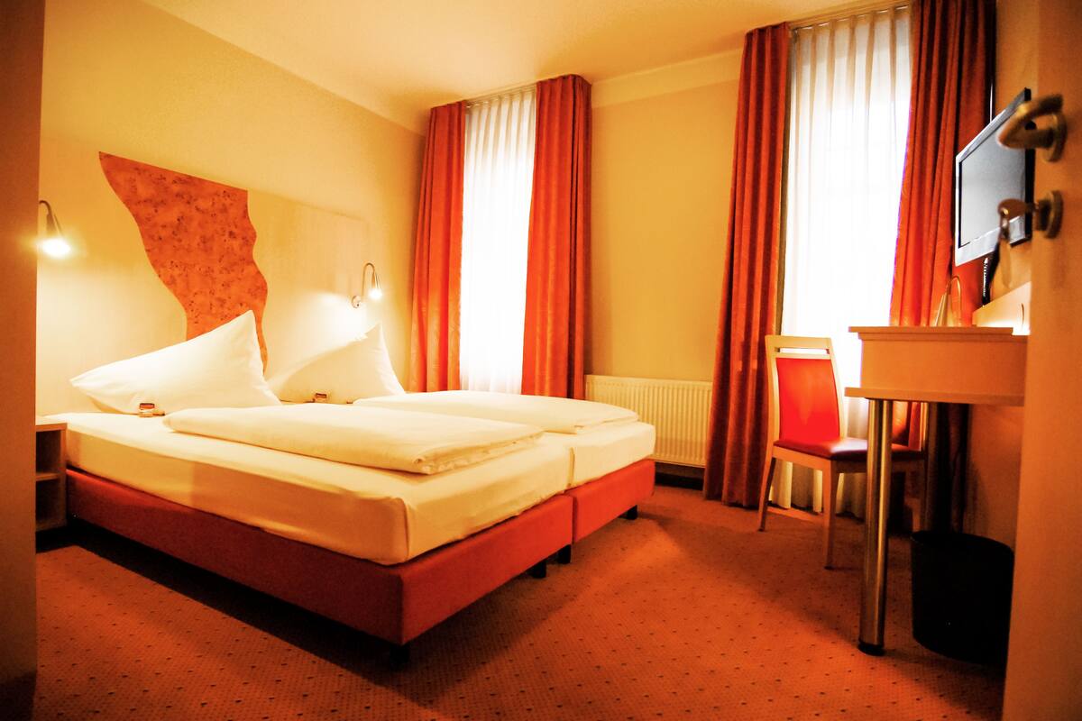 A hotel room with a bed, two bedside tables, a chair, a desk, and a television.