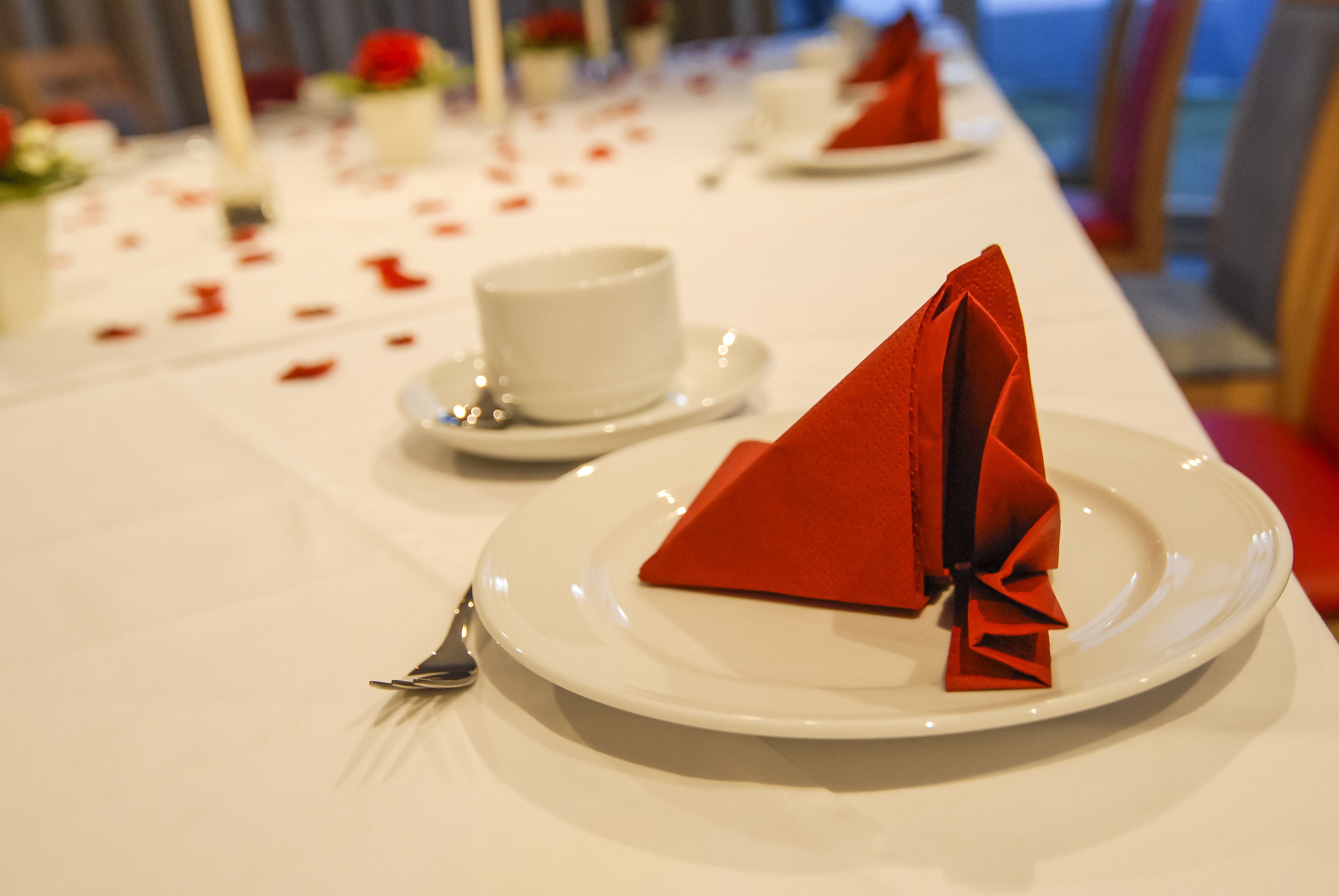 A table set with white plates, red napkins, and a white cup.