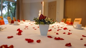 Taula amb estovell blanc, pètals de rosa vermella dispersos i un vas blanc amb una rosa vermella i verdura.