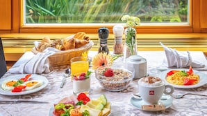 A breakfast table with various dishes, a basket of bread, a salt and pepper set, a flower vase, and a window view. - Corvin Hotel Budapest - Sissi wing (Budapest)
