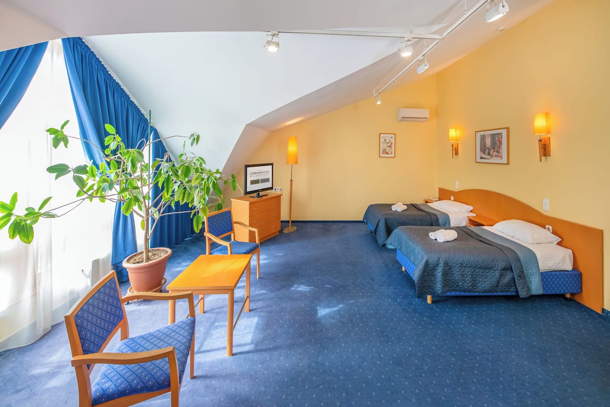 Habitación de hotel con dos camas, un escritorio, una silla, una planta en maceta y una ventana con cortinas azules.