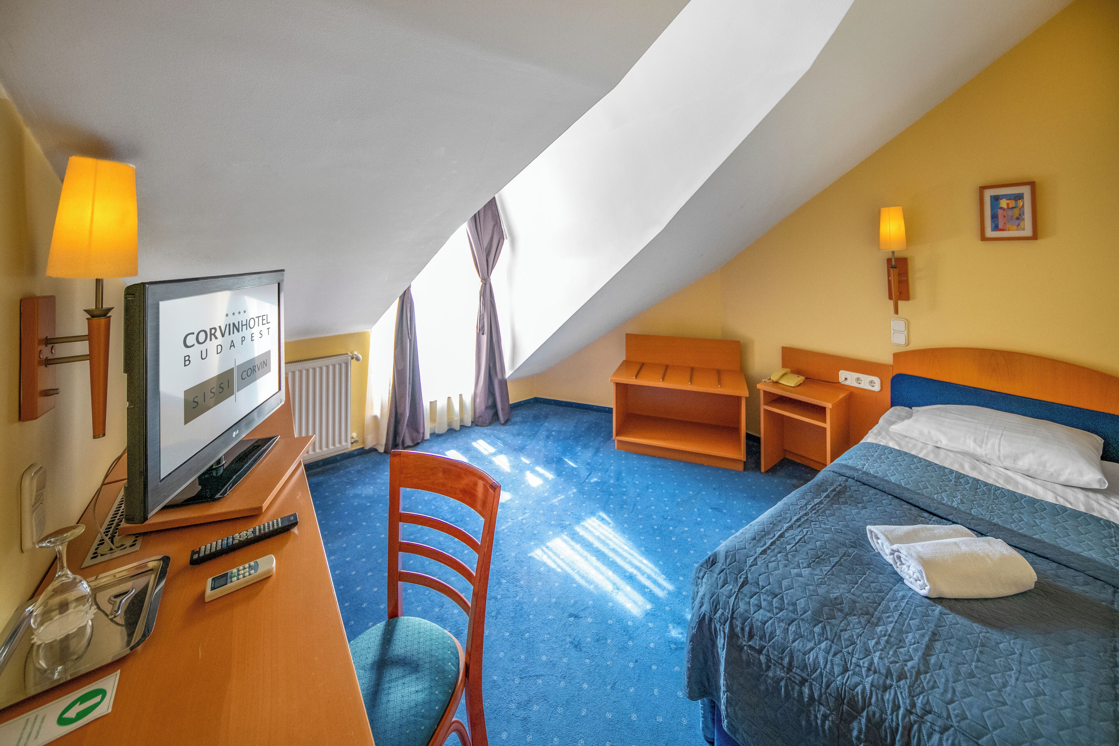 A hotel room with a bed, a desk with a TV, a chair, and a small table.