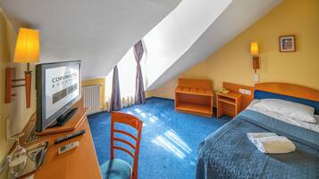 A hotel room with a bed, a desk with a TV, a chair, and a small table.