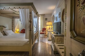 A bedroom with a four-poster bed, a television, a red chair, and a lamp. - Corvin Hotel Budapest - Sissi wing (Budapest)