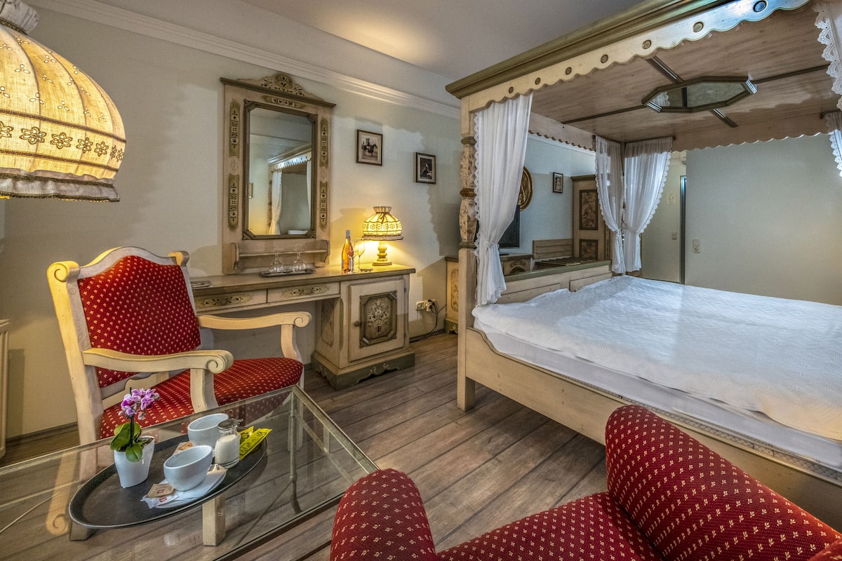 Una habitación con una cama, un escritorio, una silla, una mesa de vidrio con una bandeja de objetos y una lámpara.