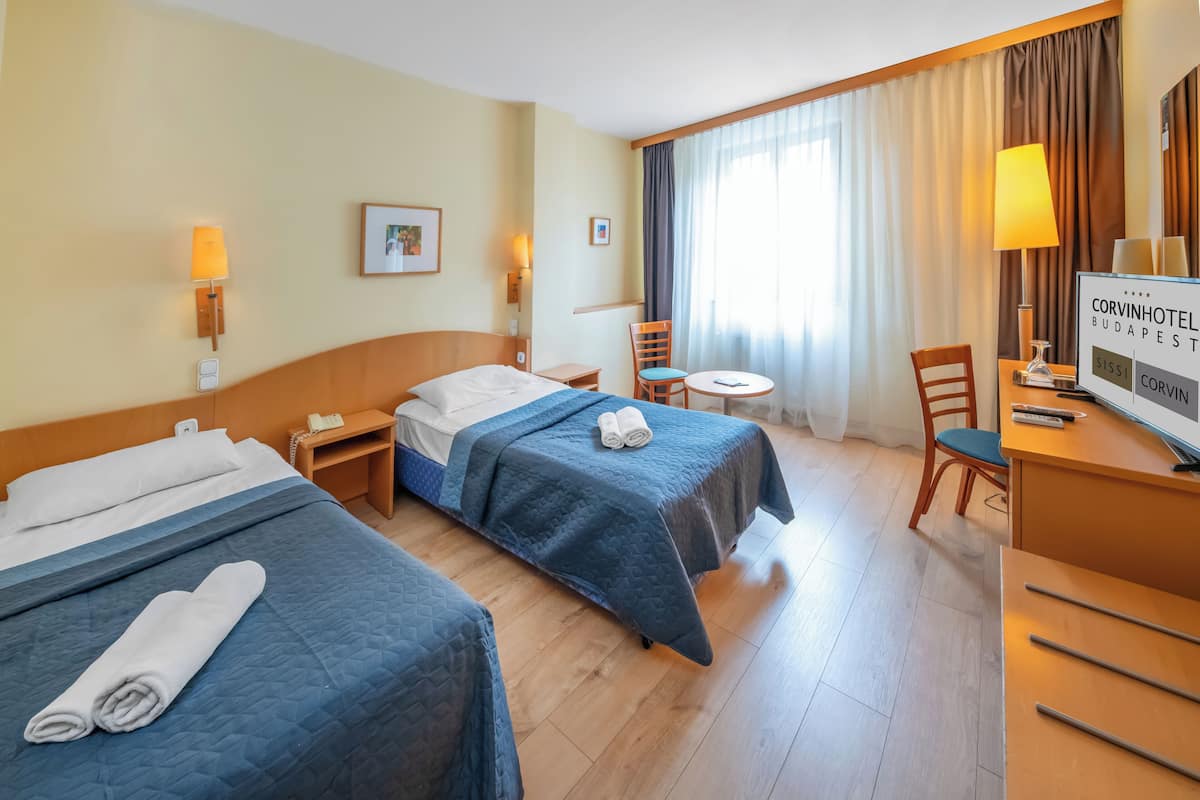 Habitación de hotel con dos camas, un escritorio, una silla, una mesita y un televisor.