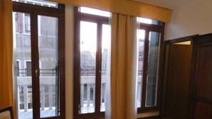 Um quarto com piso de madeira, uma cadeira e grandes janelas com cortinas.