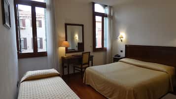 Habitación de hotel con dos camas, un escritorio, una silla, una lámpara, un espejo y dos ventanas con cortinas.