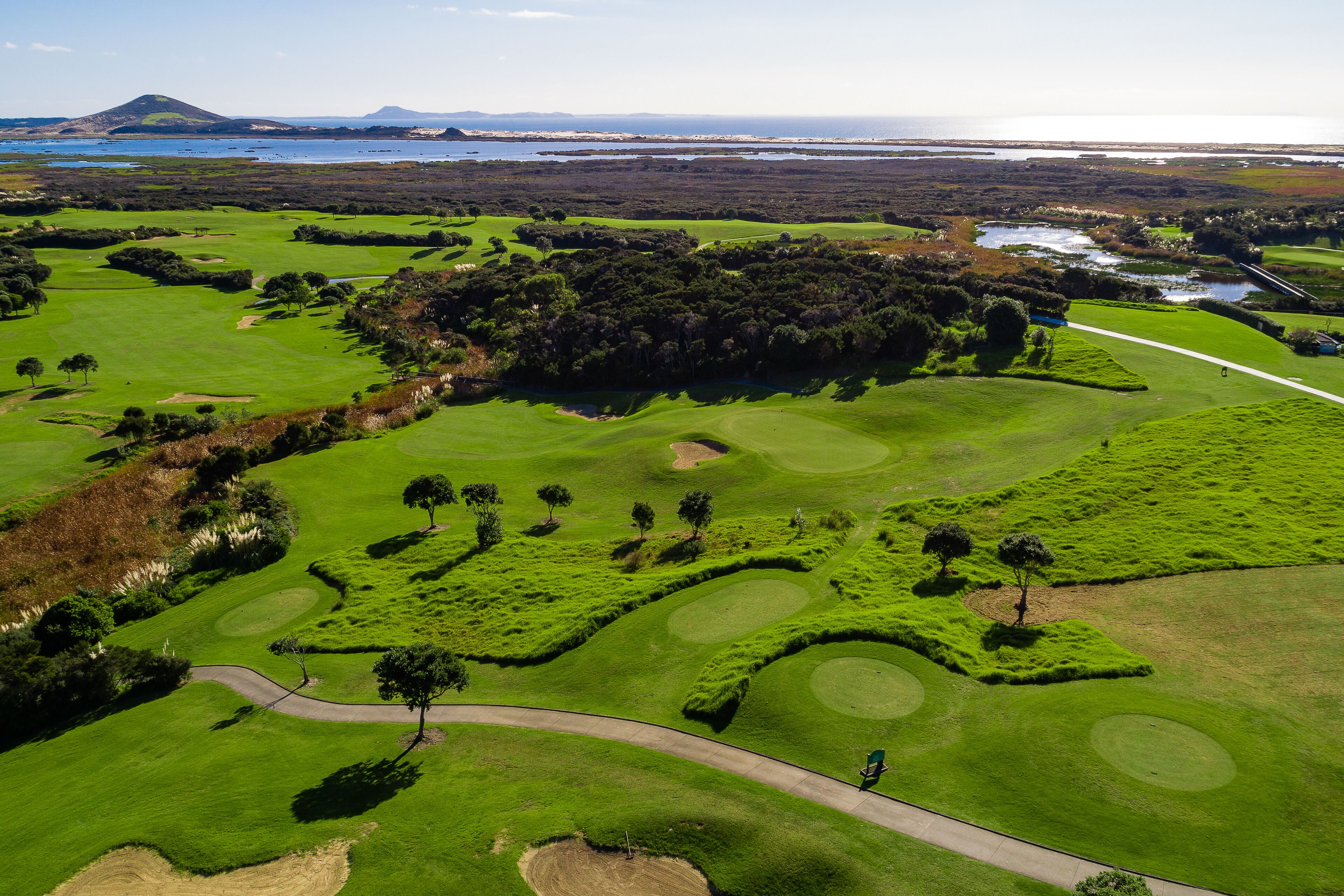 A golf course with a water body and distant mountains.