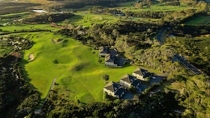 Vue aérienne d’un terrain de golf avec une grande maison entourée d’arbres et une route.