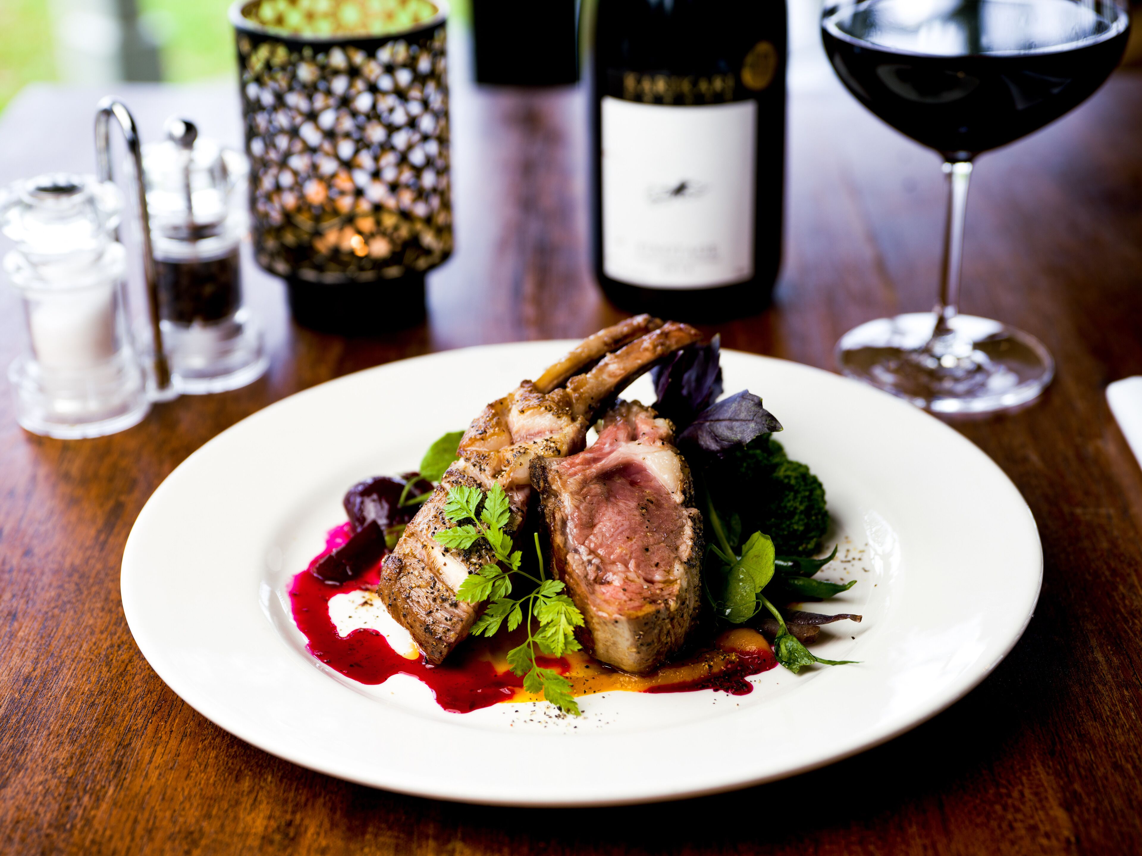 A plate of food with a glass of red wine and a bottle of wine in the background.