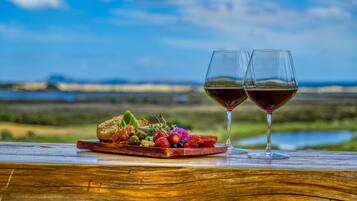 Una mesa de madera con una tabla de embutidos y dos copas de vino frente a un paisaje pintoresco.