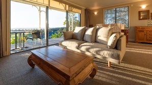Un salon spacieux, doté d’un grand canapé, d’une table basse en bois et offrant une vue imprenable sur un paysage verdoyant grâce à de grandes fenêtres.