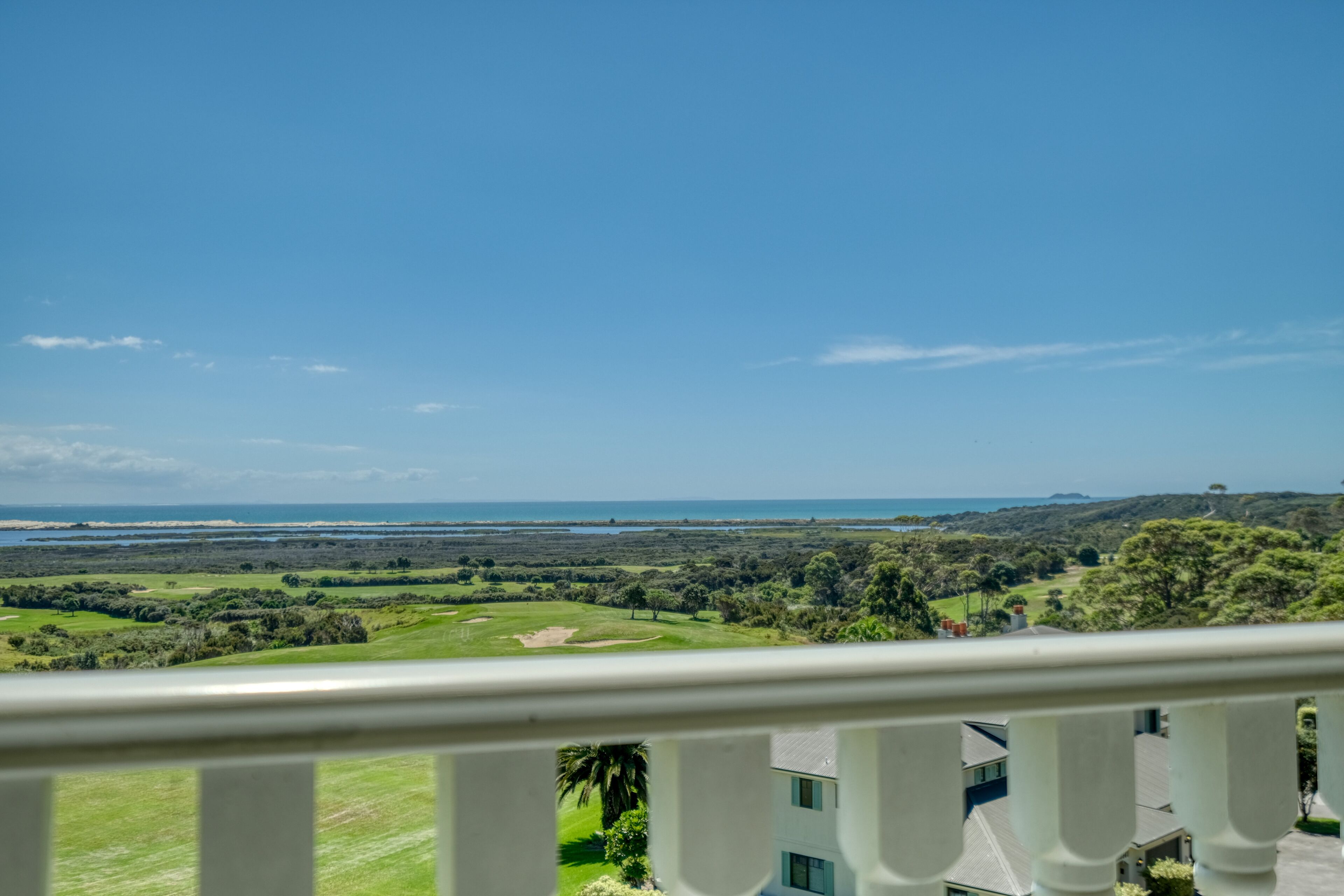 A balcony with a view of a golf course, ocean, and distant hills.
