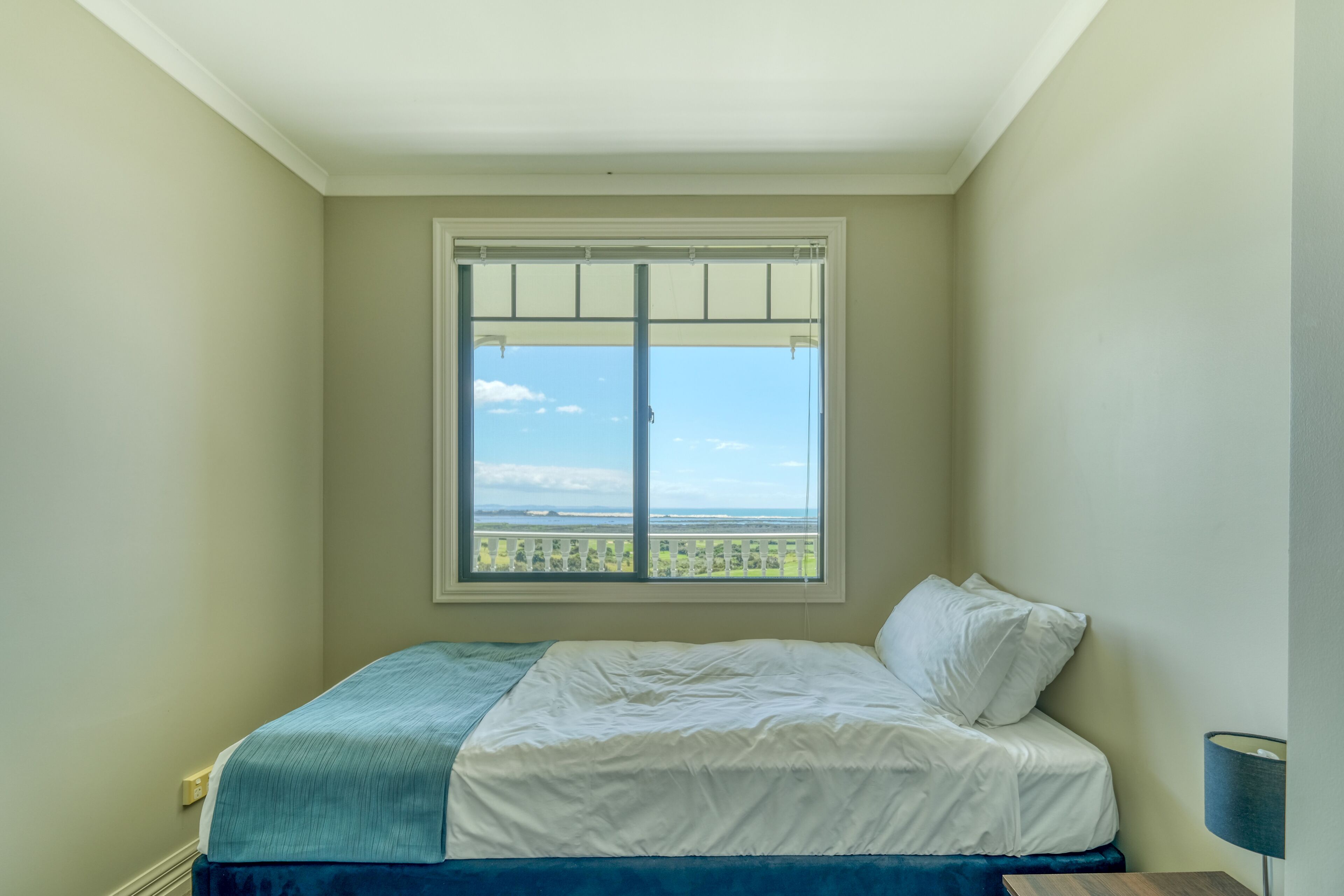 A bedroom with a bed, a window with a view, and a nightstand.