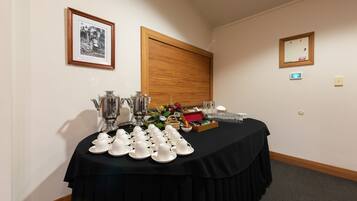 A room with a table set for tea service, framed pictures on the wall, and a window with blinds.