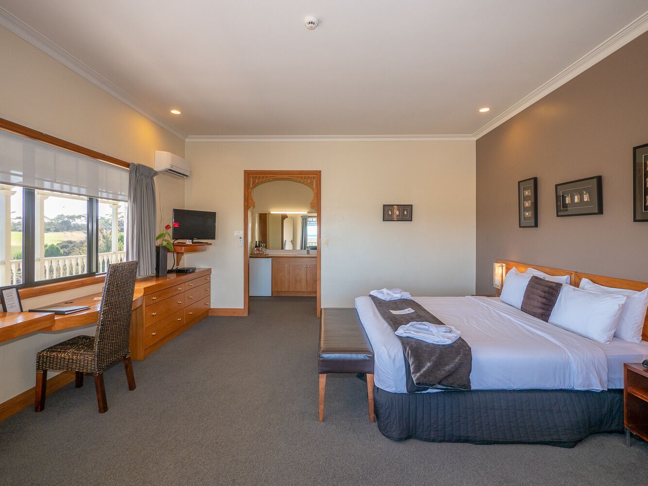 A hotel room with a large bed, a desk with a chair, a dresser, and a bathroom visible through an open door.