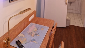 Une chambre d’hôtel dotée d’un téléviseur à écran plat fixé au mur, d’un bureau en bois avec une carte et une télécommande, et d’une salle de bain visible à travers une porte ouverte.