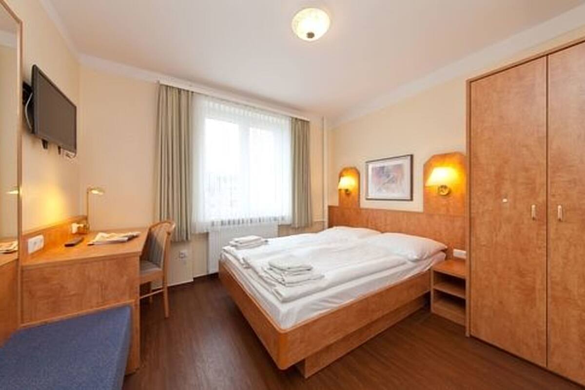 Une chambre d’hôtel équipée d’un lit, d’un bureau, d’une chaise, d’une armoire, d’une télévision et d’une fenêtre avec des rideaux.