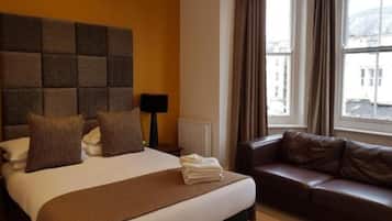 Une chambre d’hôtel avec un grand lit, une tête de lit marron, un canapé marron et une fenêtre avec des rideaux.