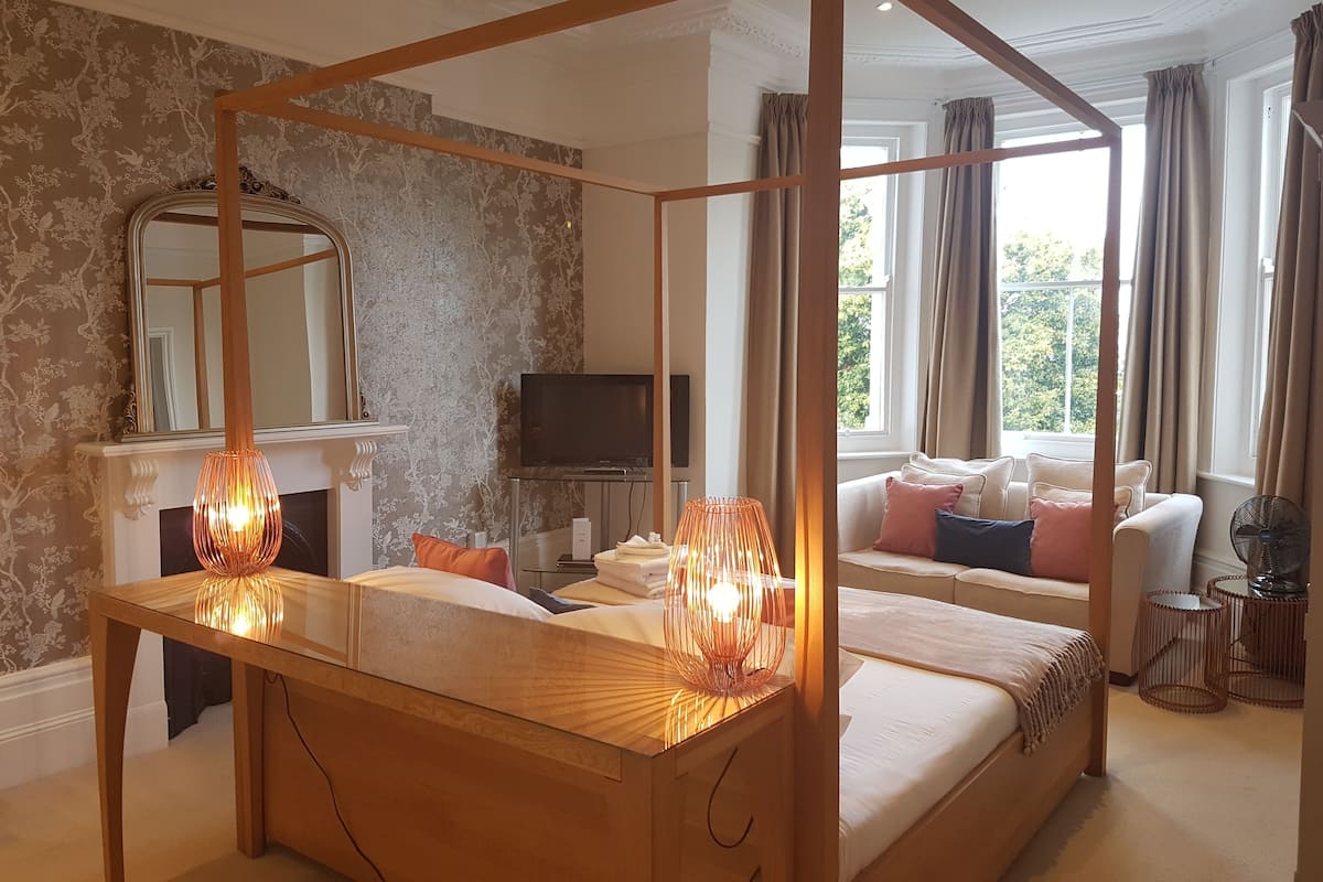 Quarto com cama de dossel, televisão, lareira e sofá.