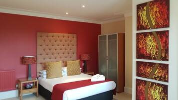 A bedroom with a tufted headboard, a bed with red and white bedding, two bedside tables with lamps, a wardrobe, and a large abstract painting on the wall.