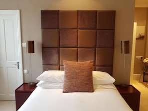 A hotel room with a large bed, a brown headboard, and a single brown pillow.
