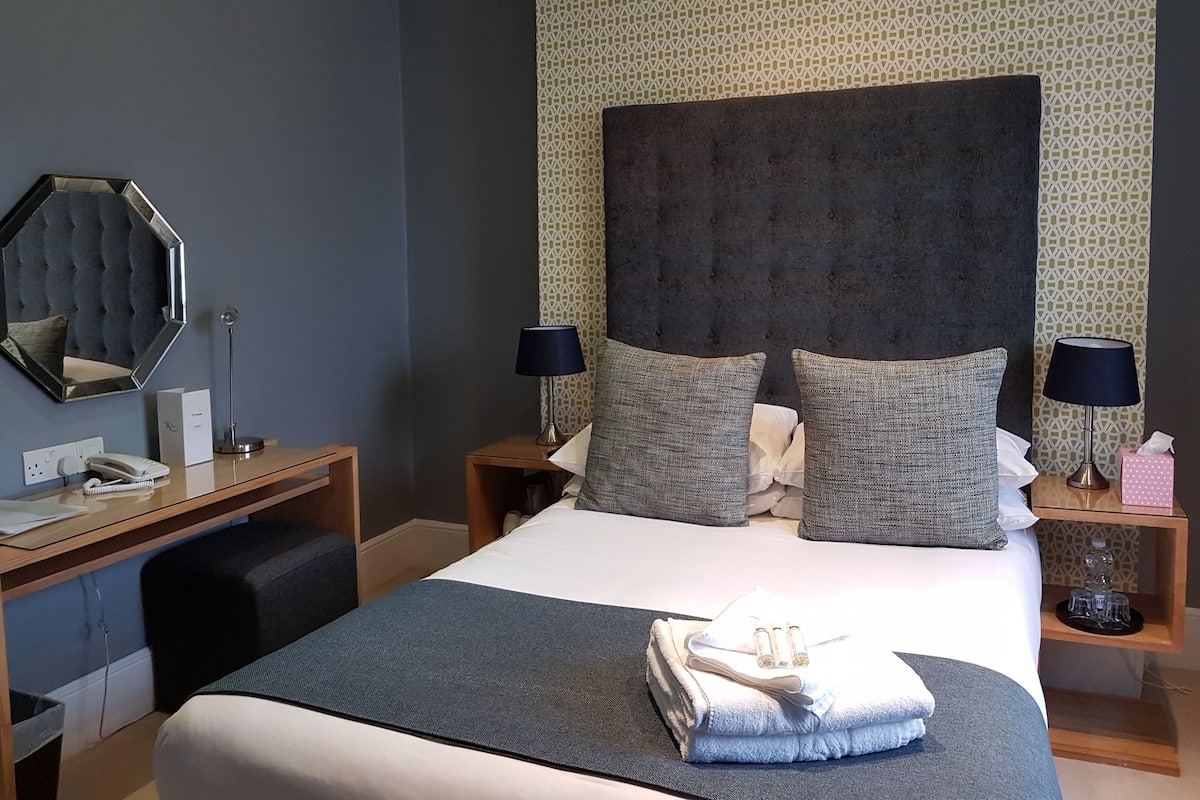 Quarto de hotel bem arrumado com uma cama grande, duas mesas de cabeceira, um espelho e papel de parede estampado.