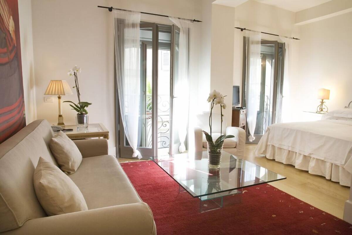 Een hotelkamer met een glazen salontafel, een bank, een bed met wit beddengoed en een rood tapijt.