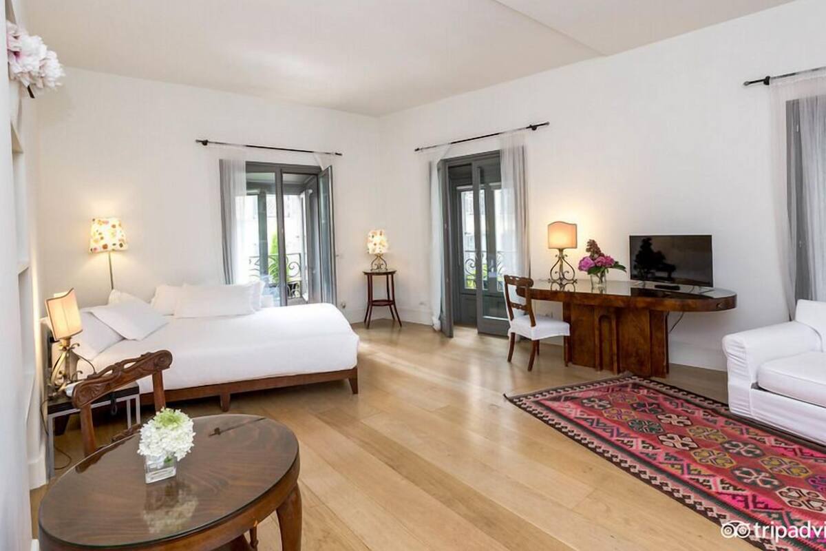 Een hotelkamer met een bed, een bureau met een televisie, een stoel en een tafeltje met een bloevas.