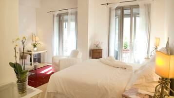 A hotel room with a large bed, a desk with a chair, a small table with a lamp, and a vase with flowers.