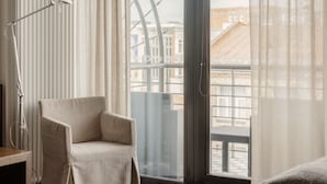 A hotel room with a large window, a chair, a bed, and a radiator. - Hotel Bergs Suites (Riga)