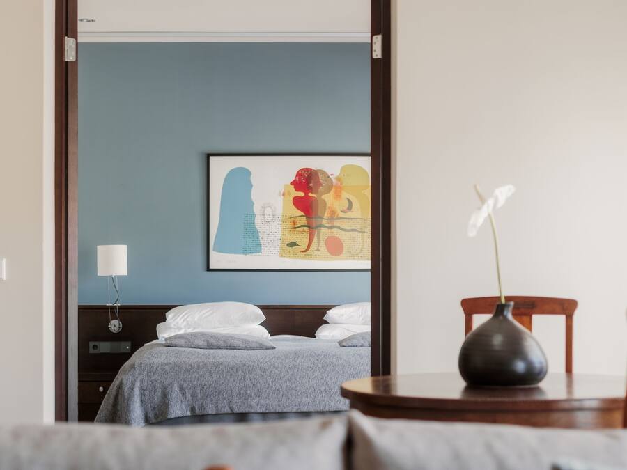 Una habitación de hotel con una cama, una mesita de noche con un florero y una lámpara de pared.